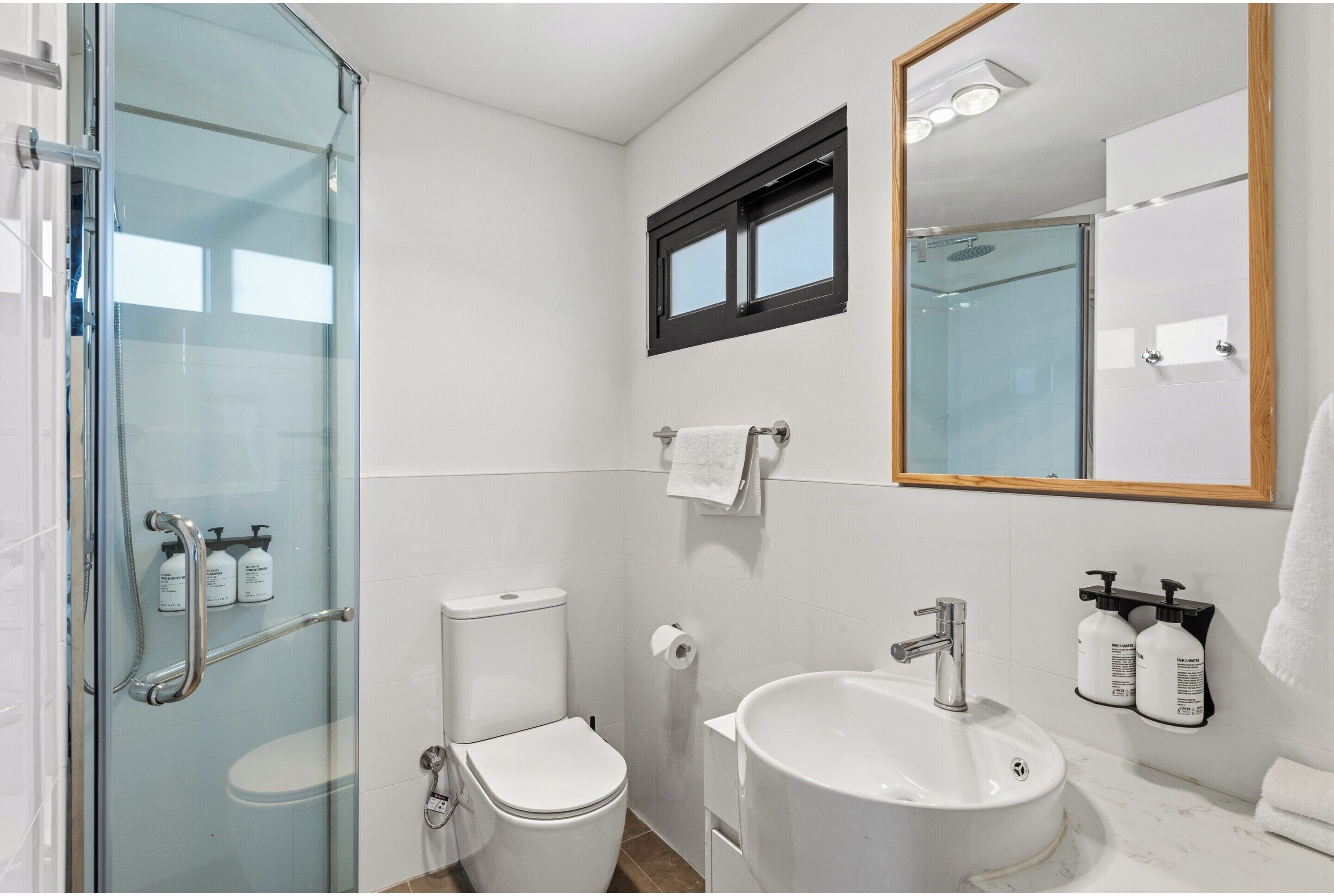 Un baño con cabina de ducha de vidrio, inodoro, lavamanos y espejo.