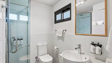 Un baño con cabina de ducha de vidrio, inodoro, lavamanos y espejo.