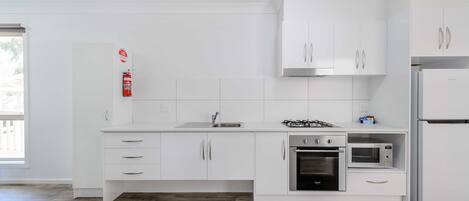 Una cocina moderna con armarios blancos, estufa a gas, horno y microondas.
