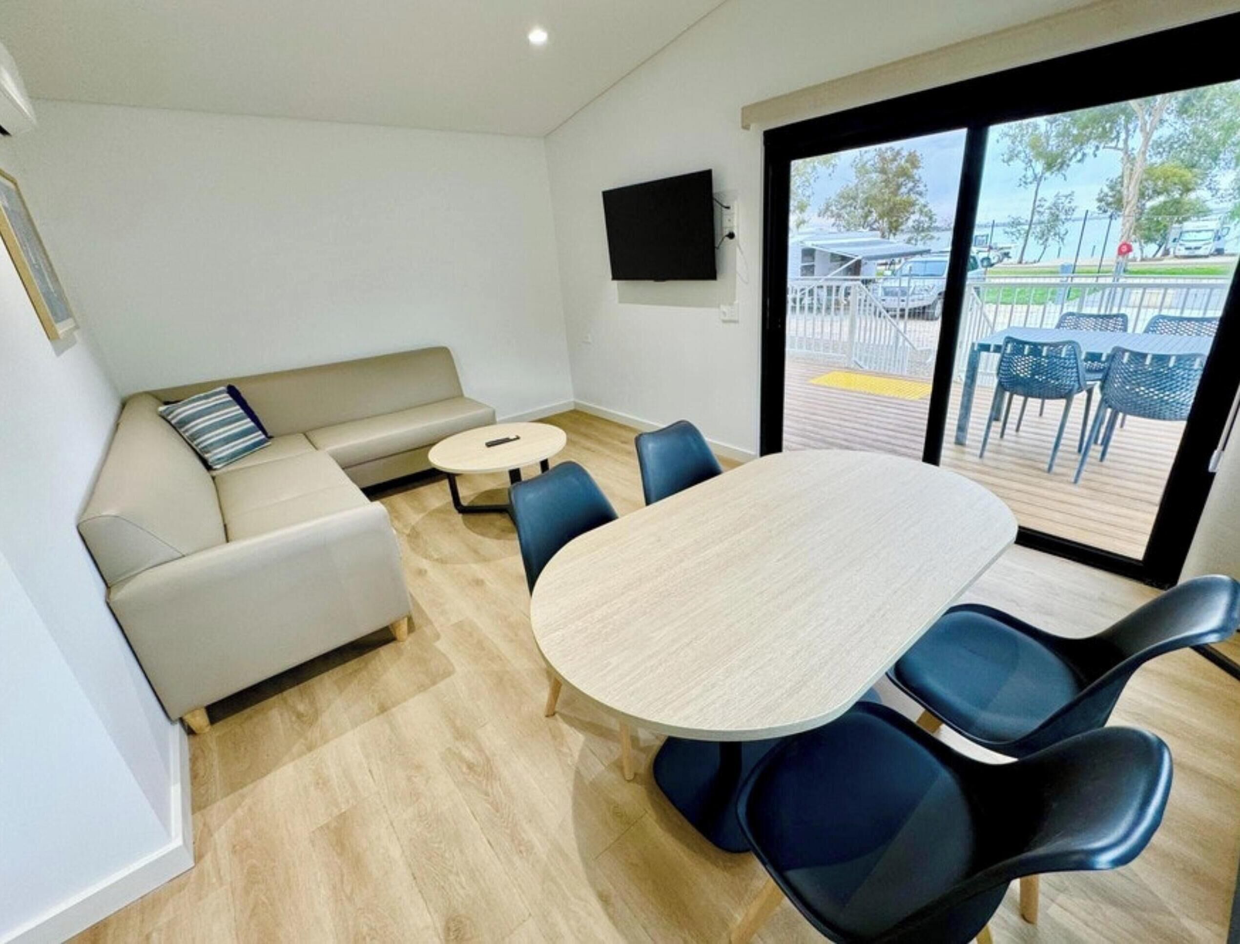 A modern room with a round table and blue chairs, a beige sofa, and a TV mounted on the wall.