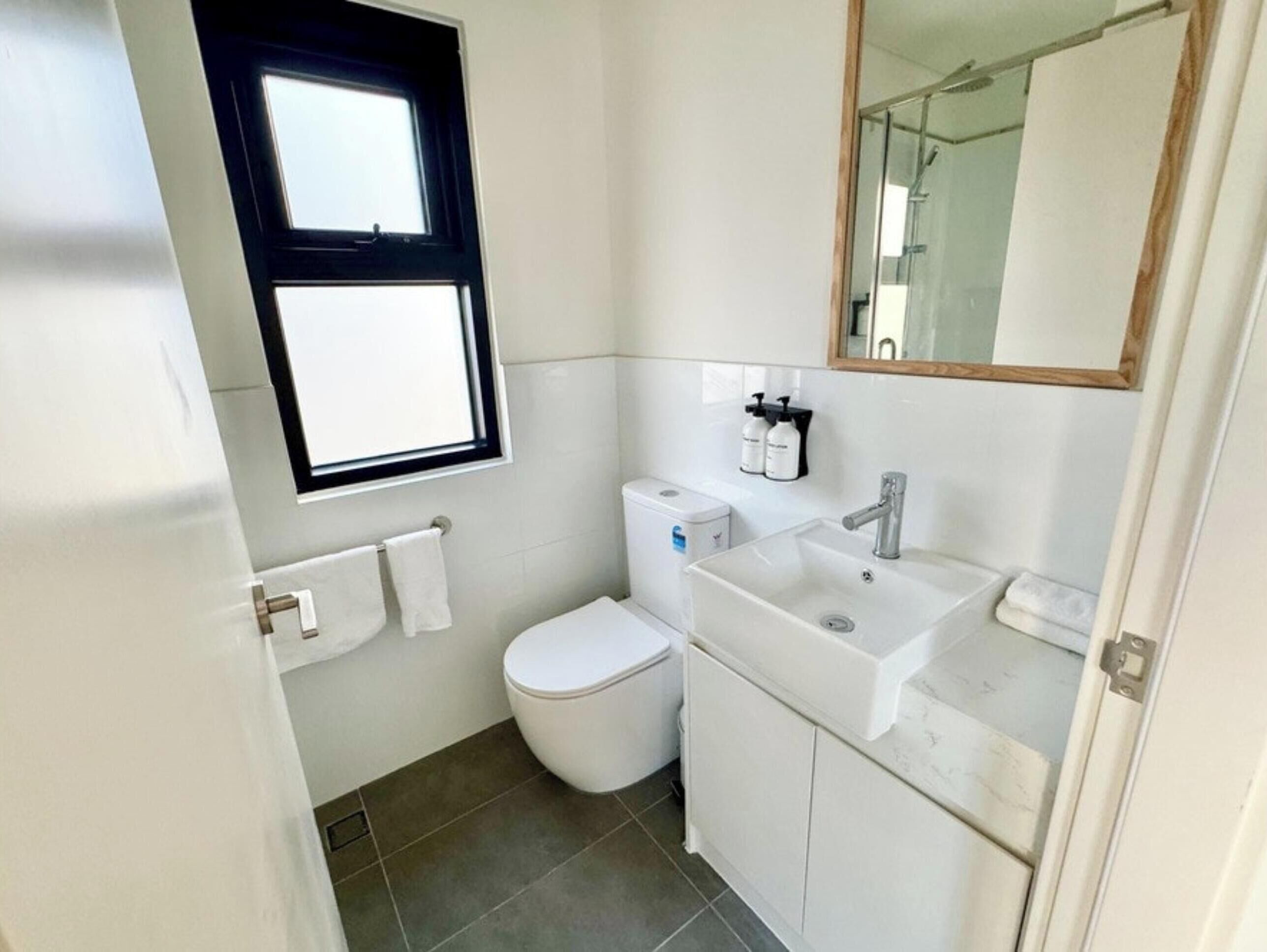 Un baño pequeño y limpio con inodoro, lavamanos y ventana sobre el inodoro.