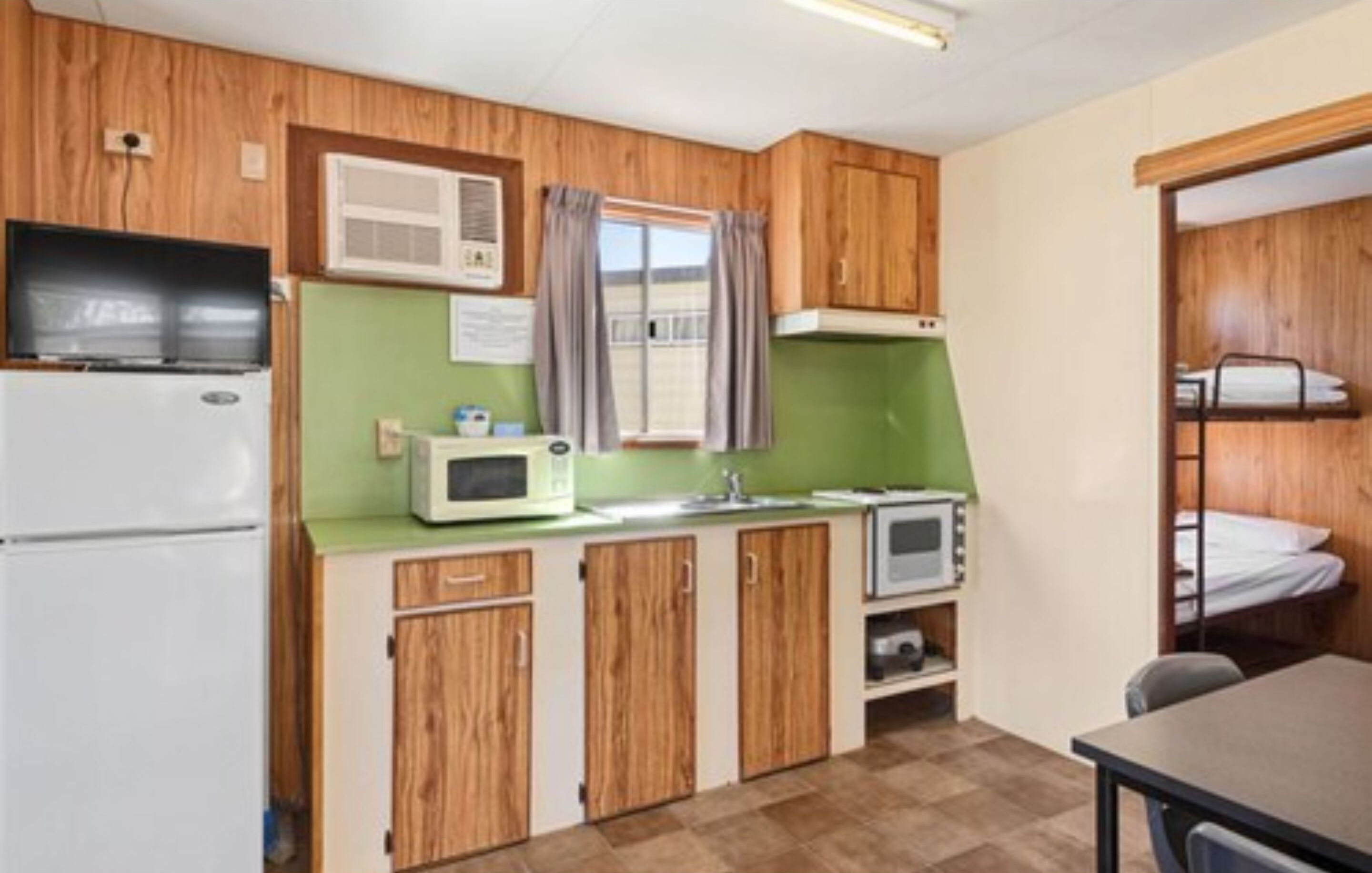 A compact kitchen with wooden cabinets, a microwave, a refrigerator, and a sink.
