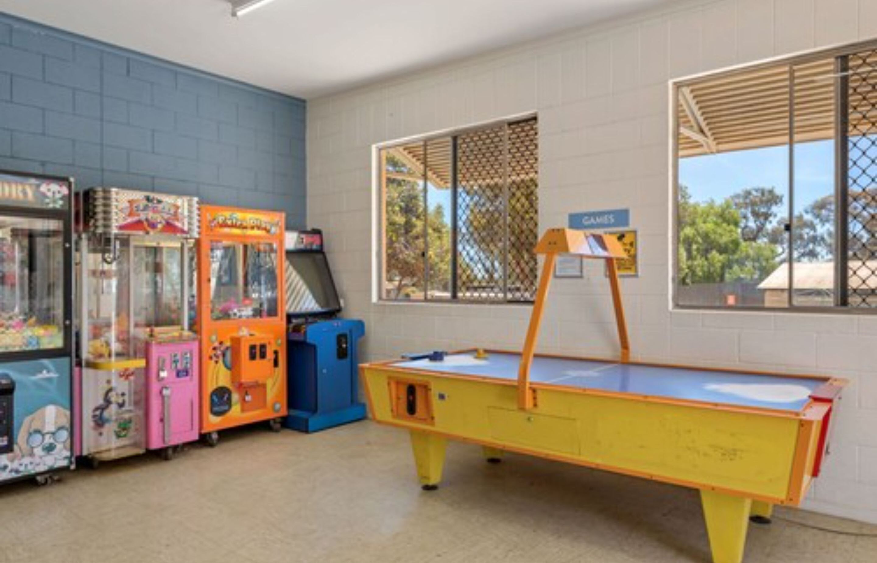 A room with arcade games, a ping pong table, and a window with a view of trees.