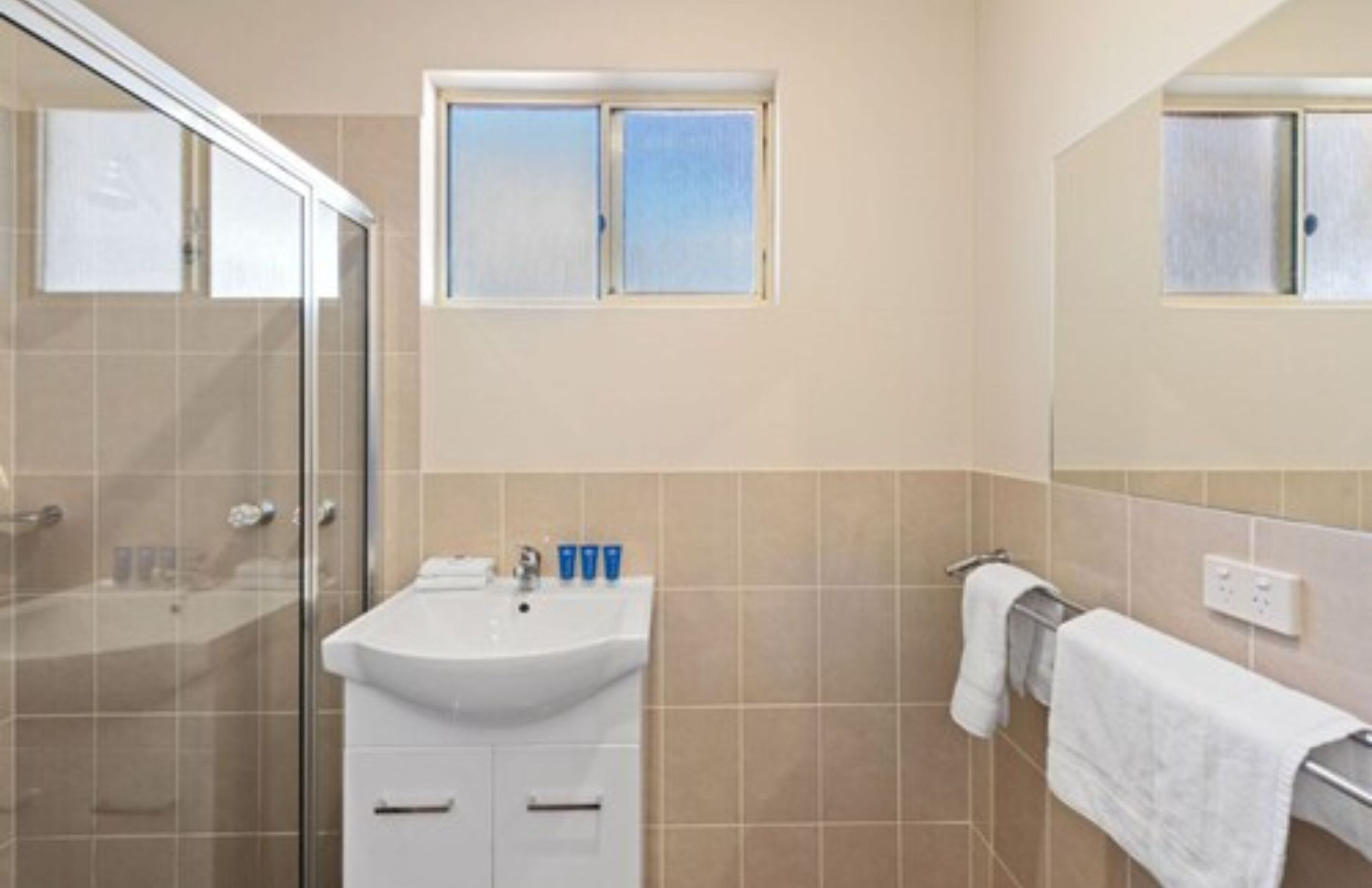 Un baño con cabina de ducha de vidrio, un lavabo con espejo y una ventana sobre el lavabo.