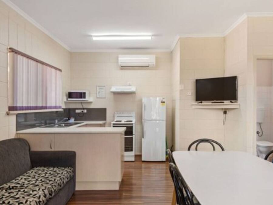 A compact kitchen with a dining area, a sofa, and a TV mounted on the wall.