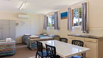 Une pièce compacte avec une kitchenette, deux lits dotés de draps colorés, une table à manger avec des chaises et une fenêtre avec des rideaux.