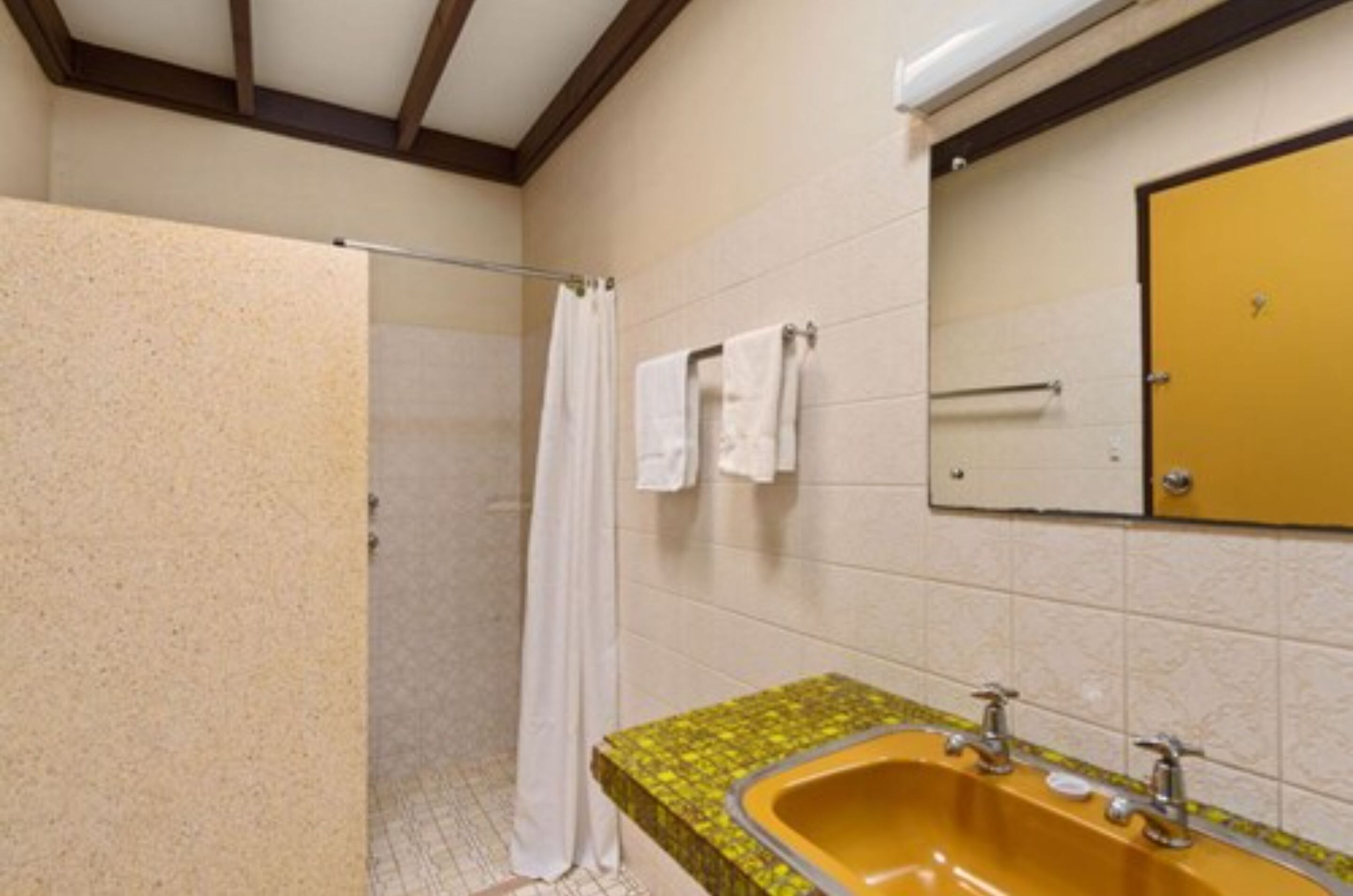 Un baño con ducha, un lavamanos amarillo y un espejo encima.