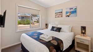 Habitación de hotel con cama, ventana con vistas, ventilador de techo y obras de arte en la pared.