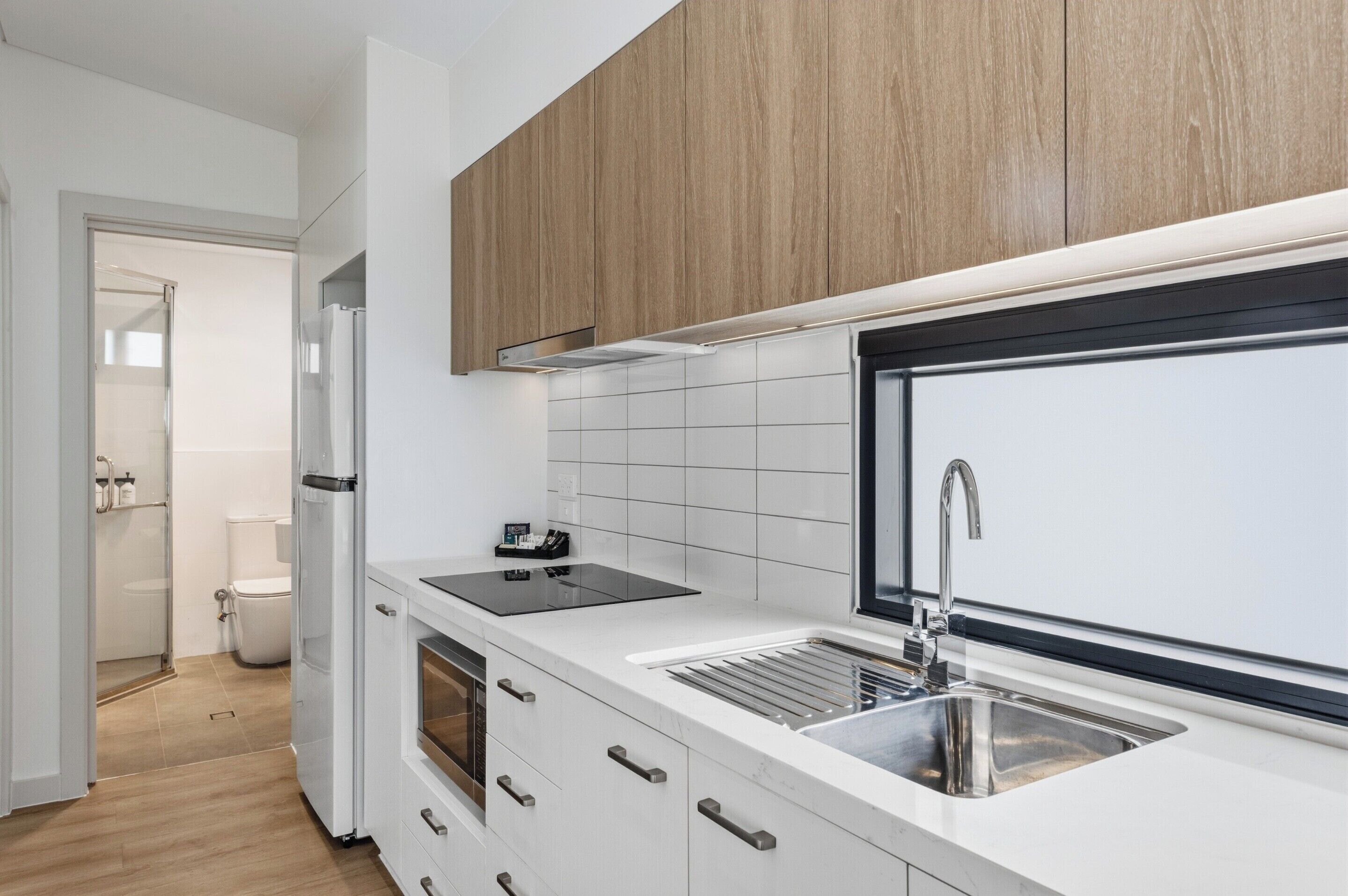 A modern kitchen with white cabinetry, a black countertop, a stainless steel sink, and a built-in oven.