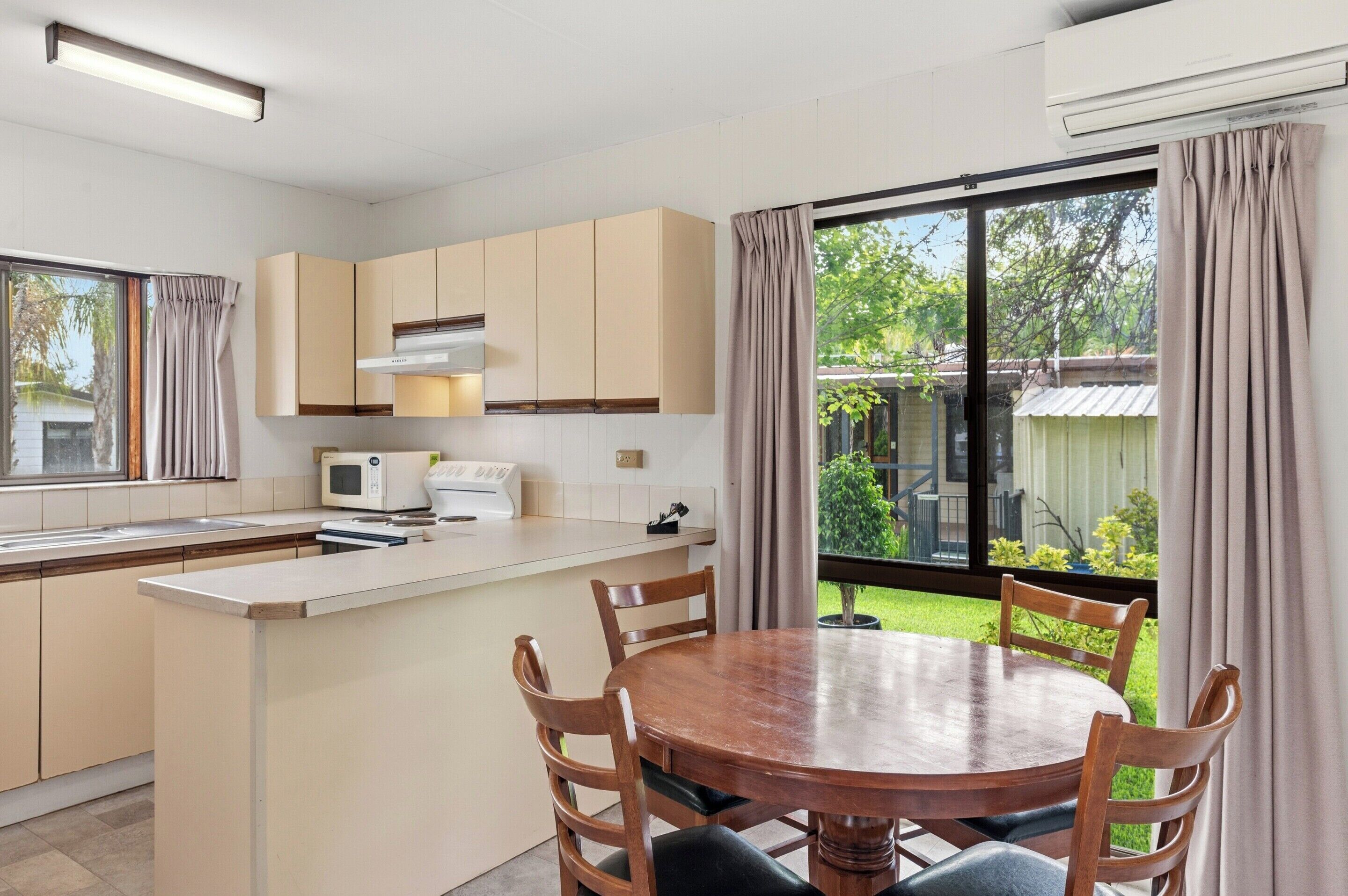 A modern kitchen with a dining area, large windows, and a view of a garden.