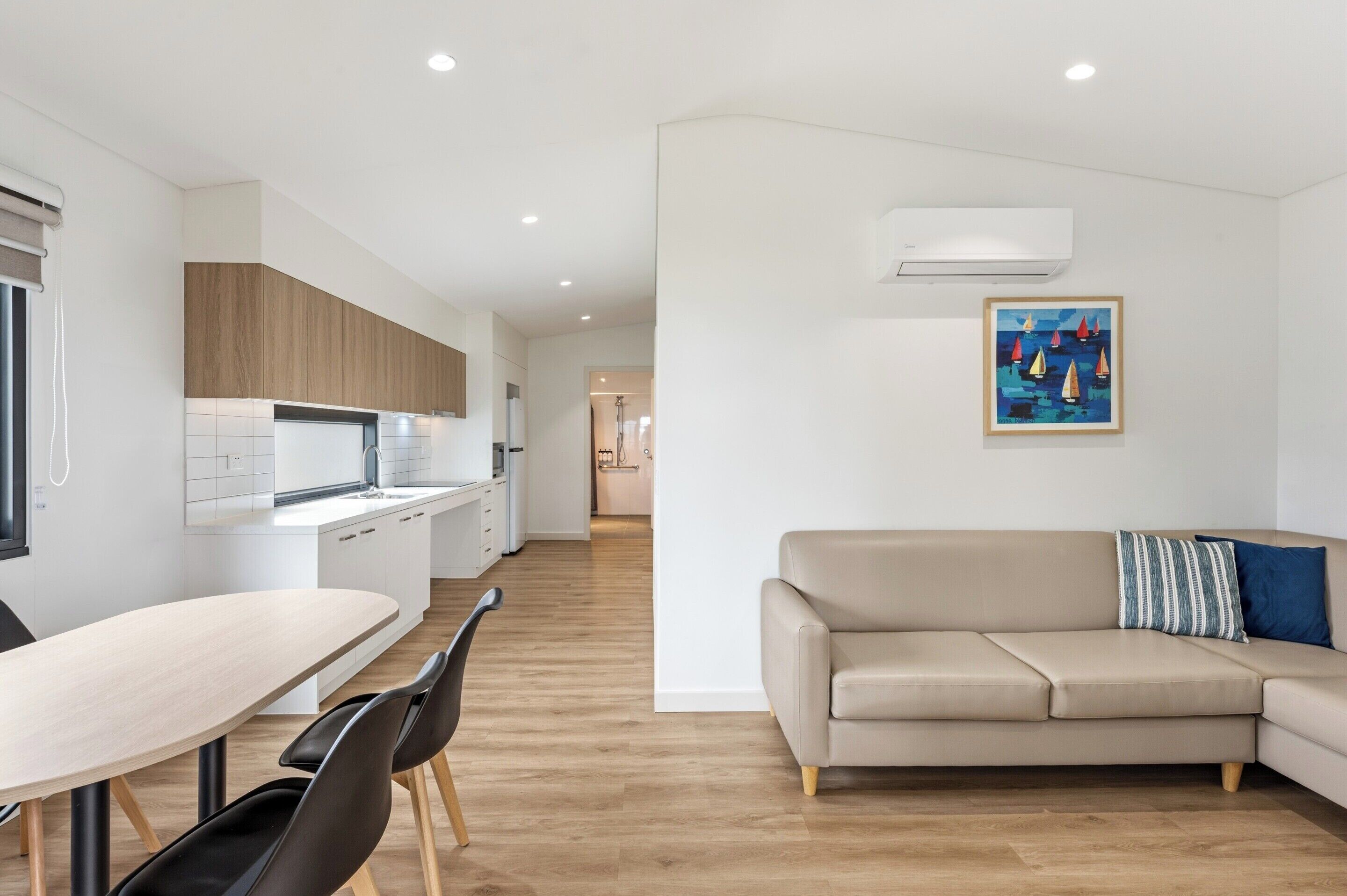 A modern kitchen with white cabinets, a dining table with chairs, a beige sofa, and a painting on the wall.