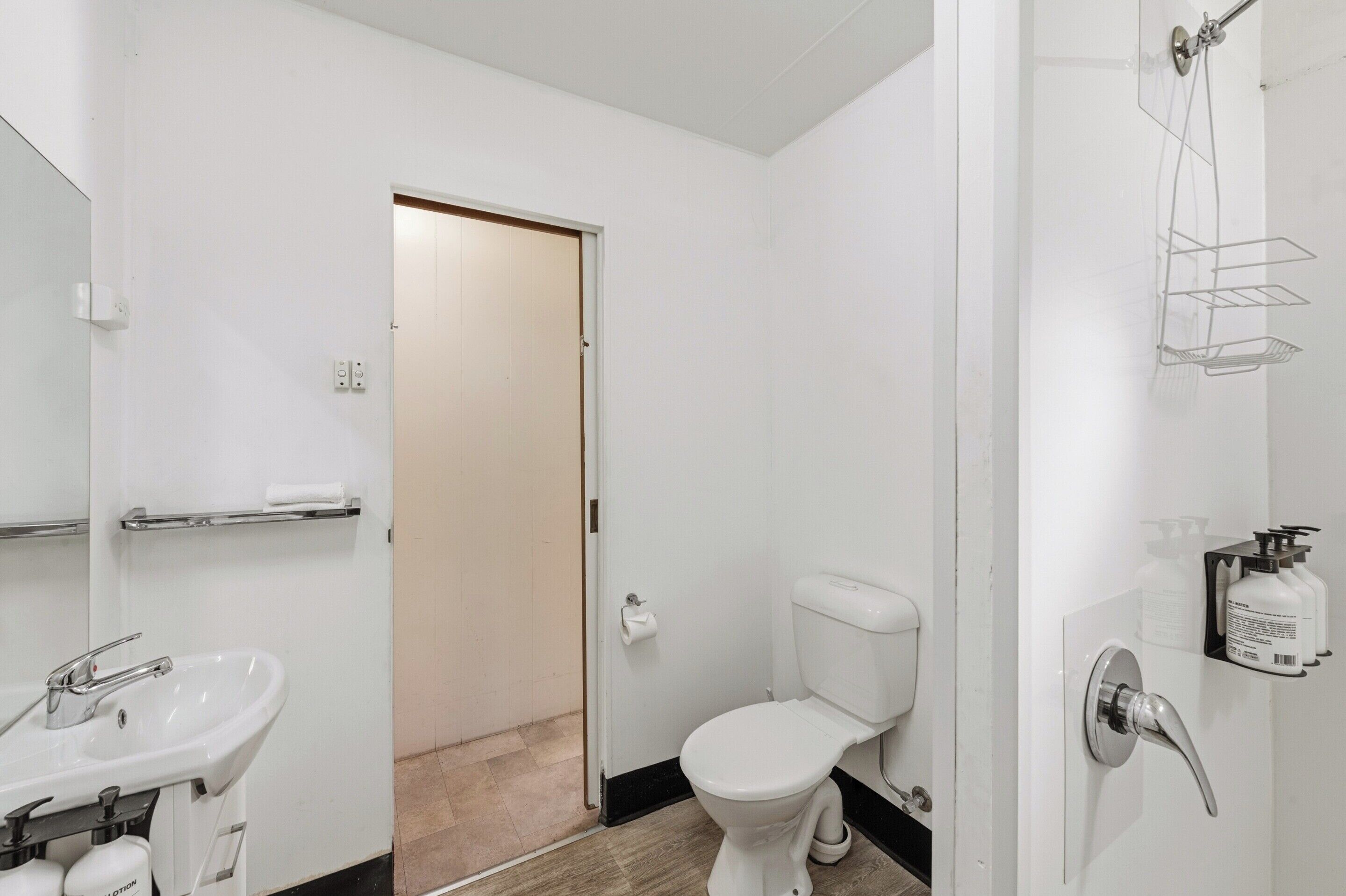 A bathroom with a white sink, toilet, and shower. There is a towel rack and a soap dispenser on the wall.