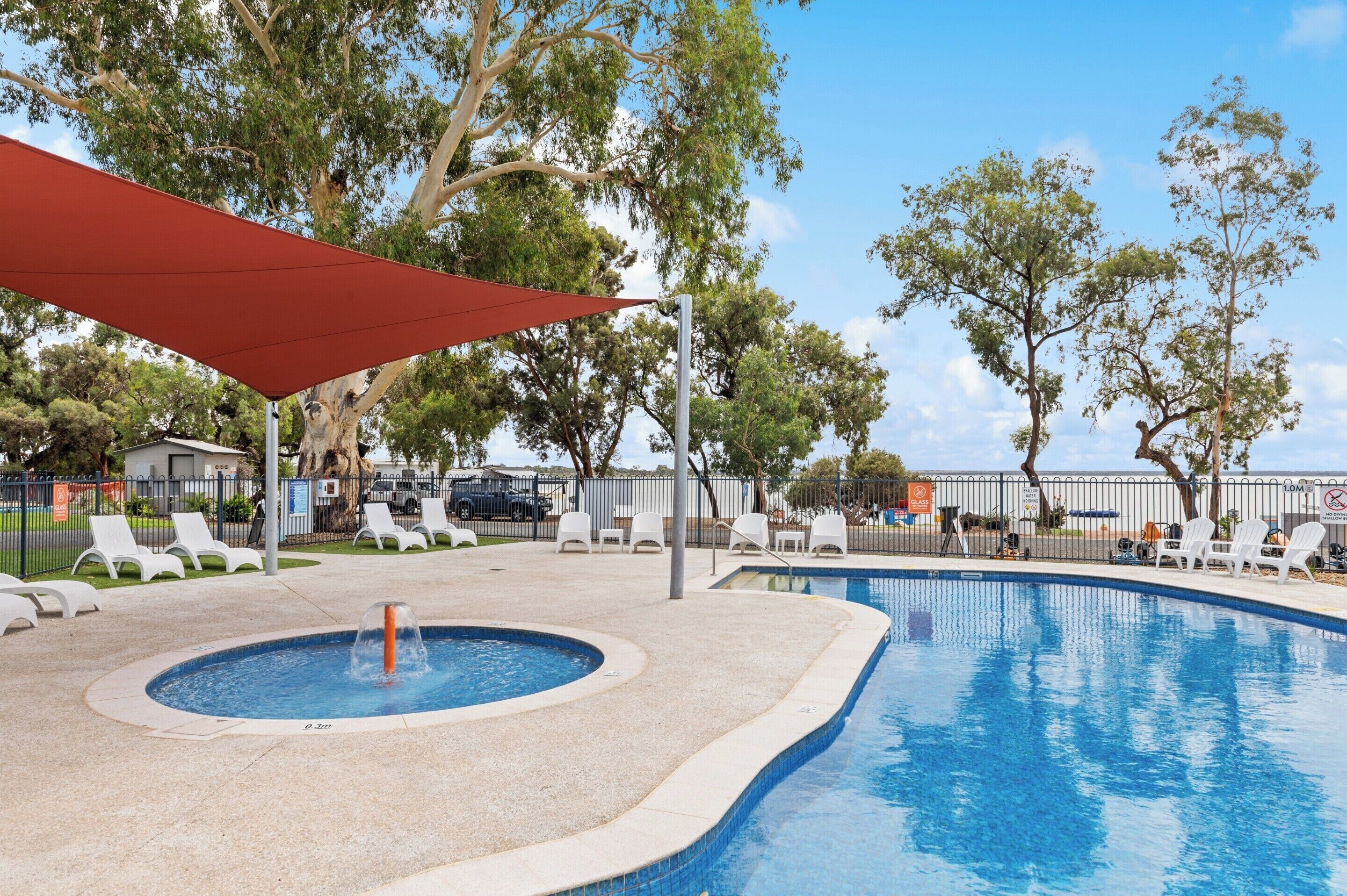 Une piscine avec un jacuzzi, entourée de chaises longues blanches et surmontée d’un auvent rouge.
