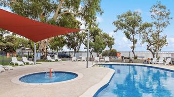Une piscine avec un jacuzzi, entourée de chaises longues blanches et surmontée d’un auvent rouge.