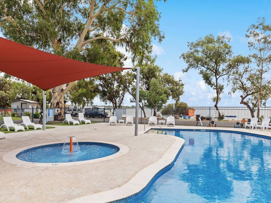 Une piscine avec un jacuzzi, entourée de chaises longues blanches et surmontée d’un auvent rouge.