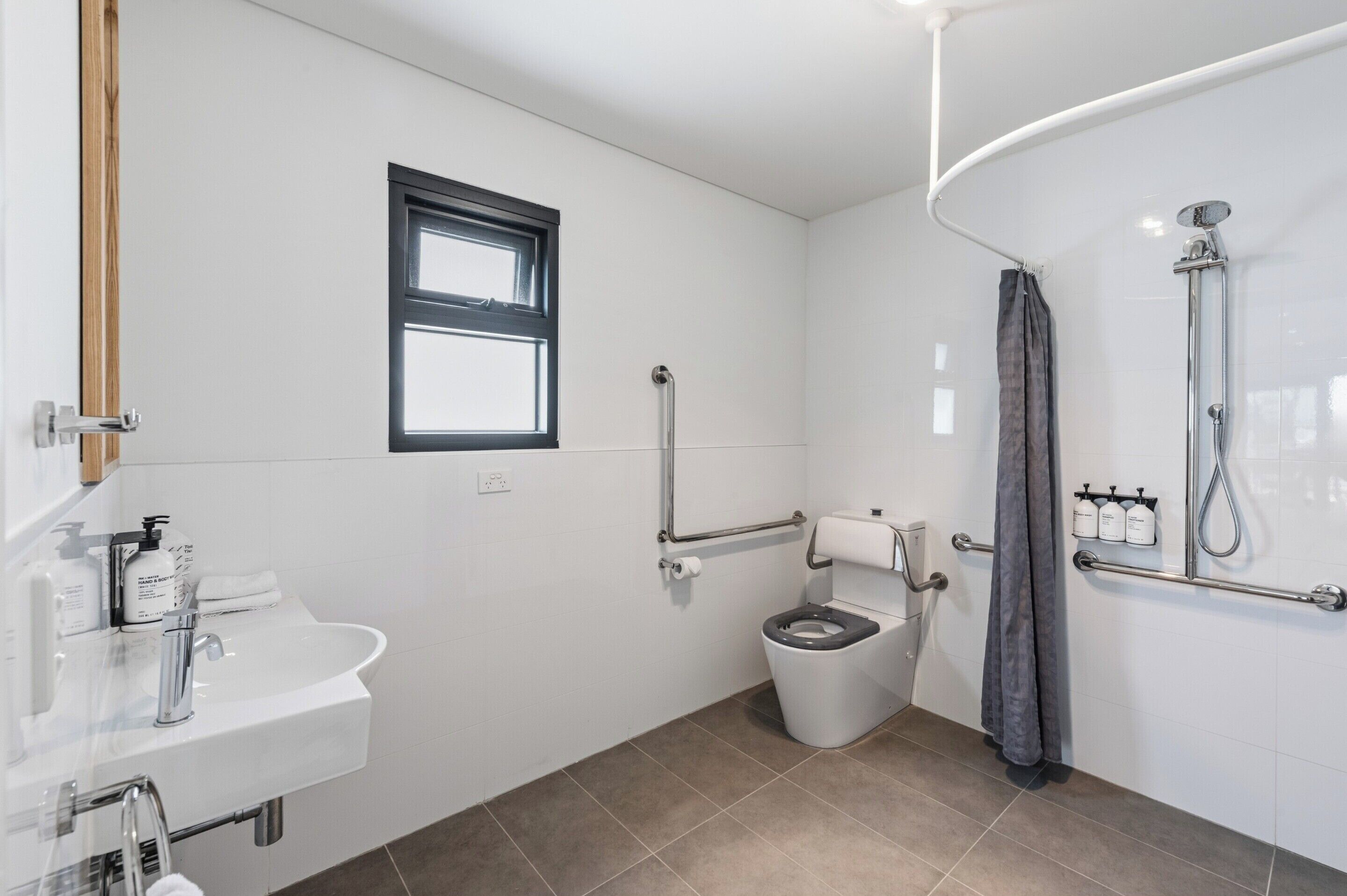 A modern bathroom with a sink, toilet, shower, and window.