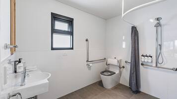 A modern bathroom with a sink, toilet, shower, and window.