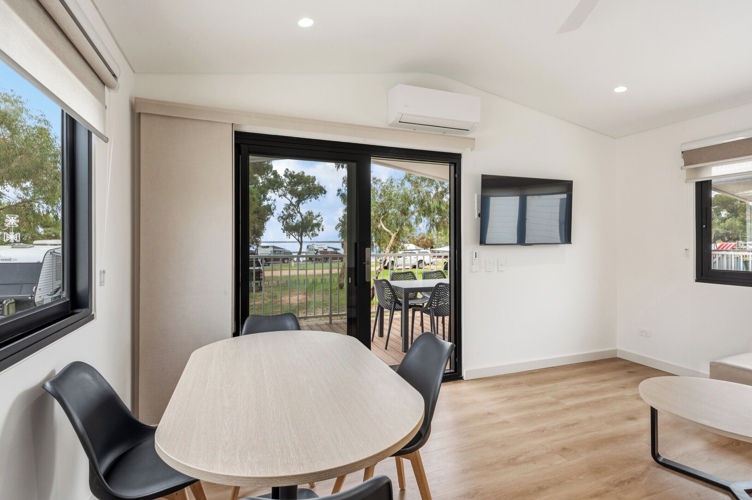 A modern room with a large window, a round table, and a balcony with outdoor furniture.