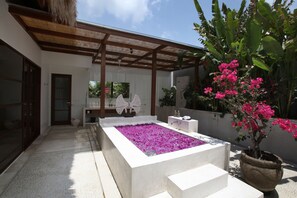 A modern outdoor bathroom with a large rectangular pool filled with pink flowers, surrounded by steps and a potted plant. - Nyaman Villas (Seminyak)