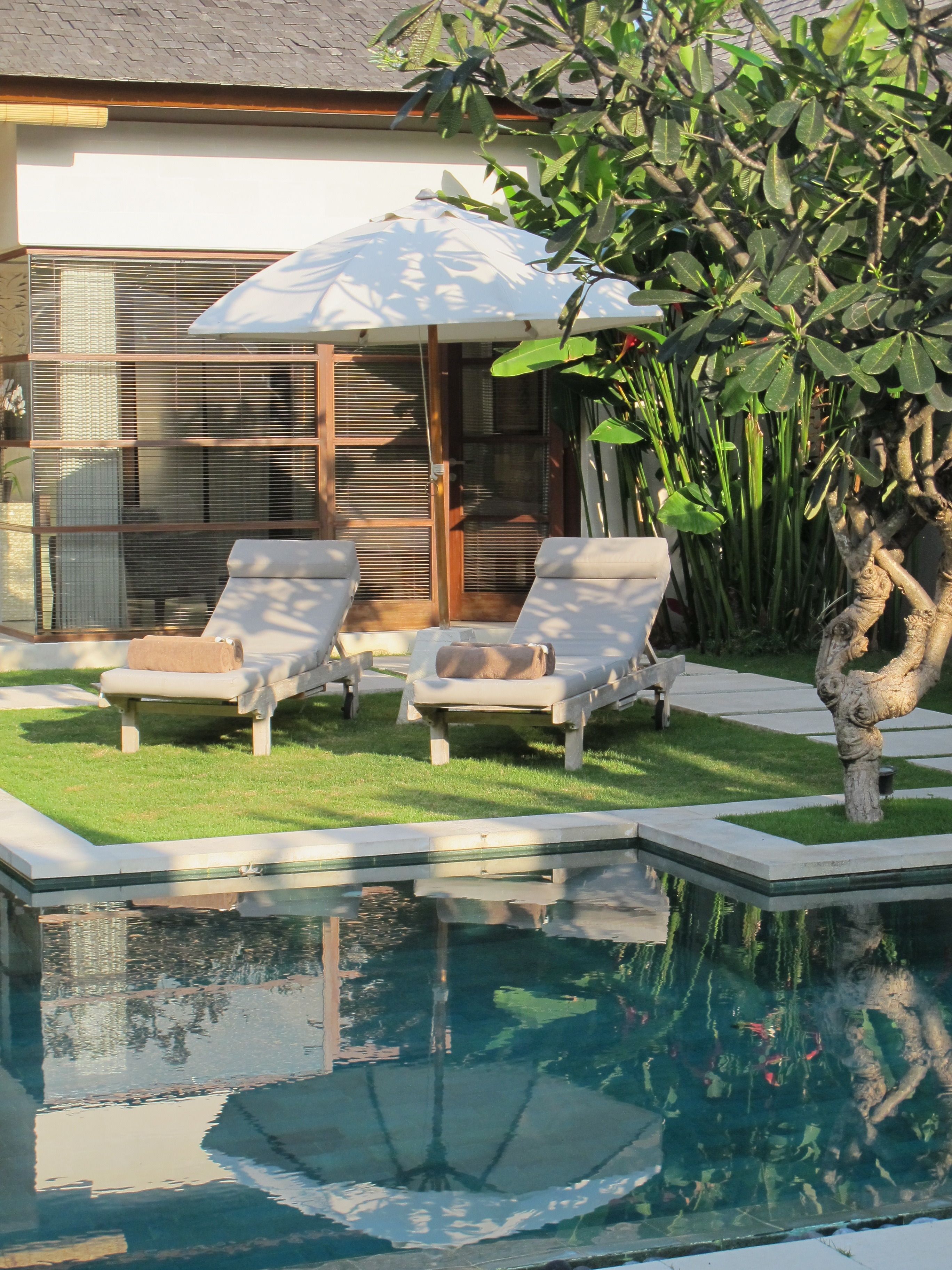 A pool area with two lounge chairs, a small umbrella, and a stone sculpture.