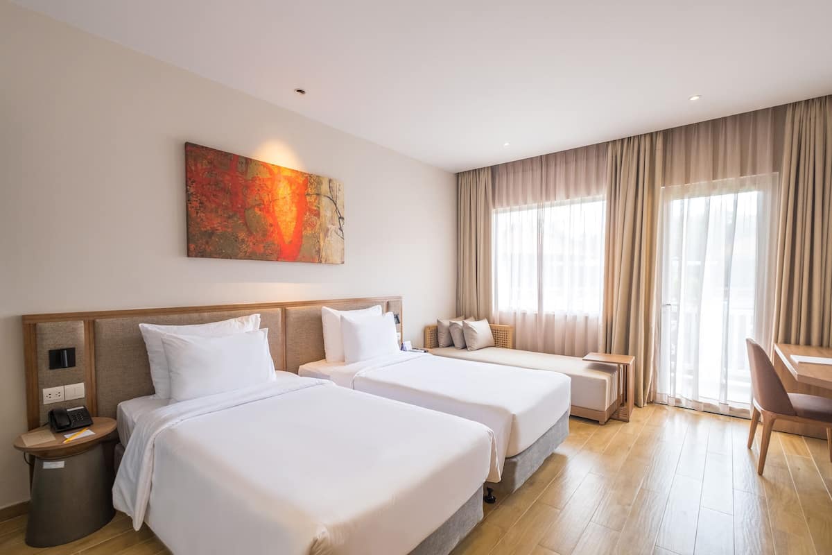 Habitación de hotel con dos camas, un escritorio y una silla. Hay un cuadro en la pared y una ventana con cortinas.