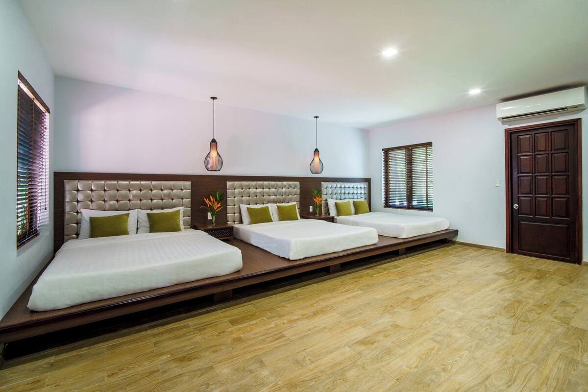 Habitación de hotel con una cama grande, un sofá cama y una mesita. Hay dos lámparas colgantes del techo.