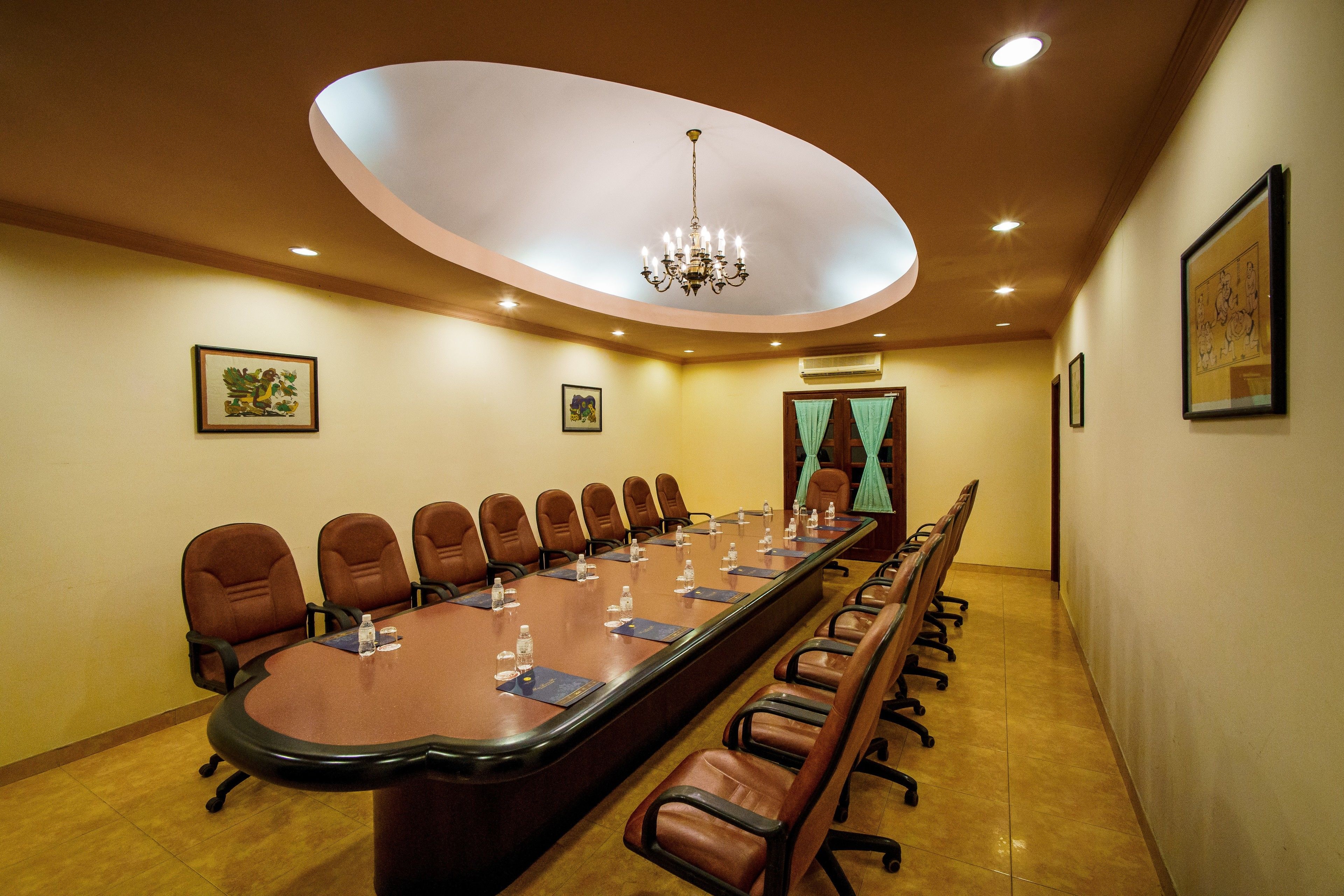 A conference room with a long table, brown leather chairs, and a chandelier.