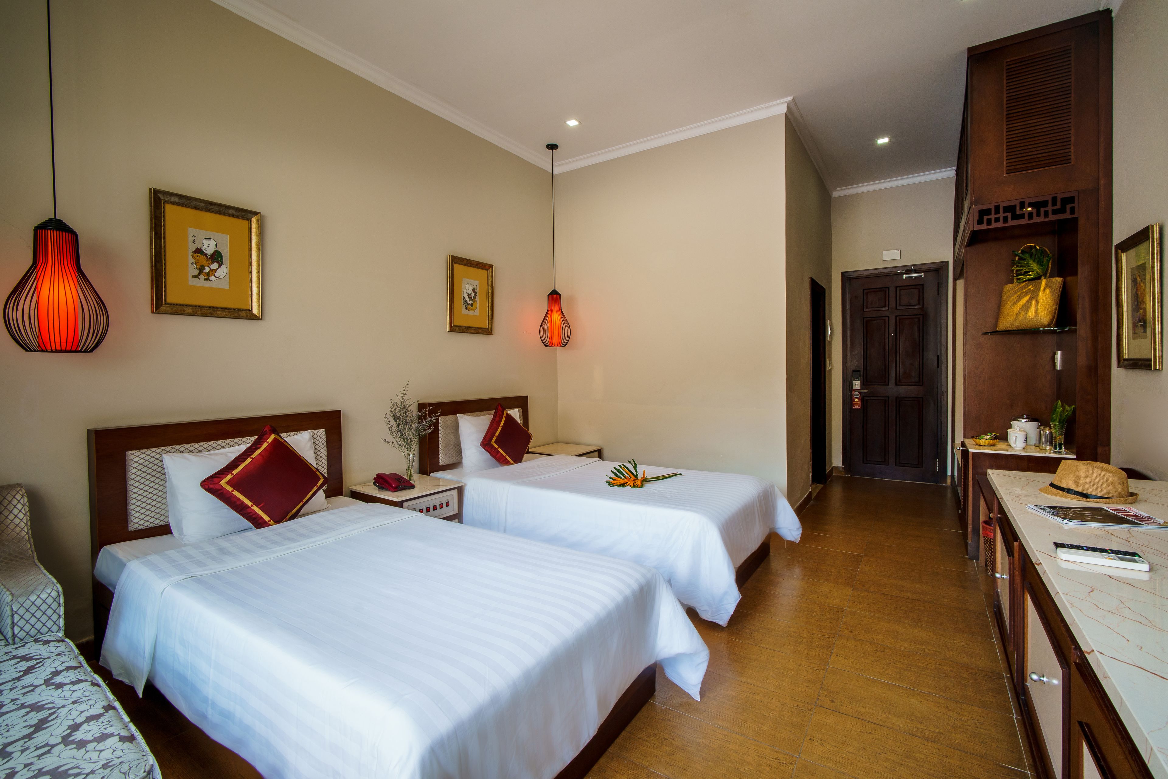Ein Hotelzimmer mit zwei Betten, einem Holz-Kopfstück, einem Schreibtisch mit Hut und einem Regal mit Dekoration.