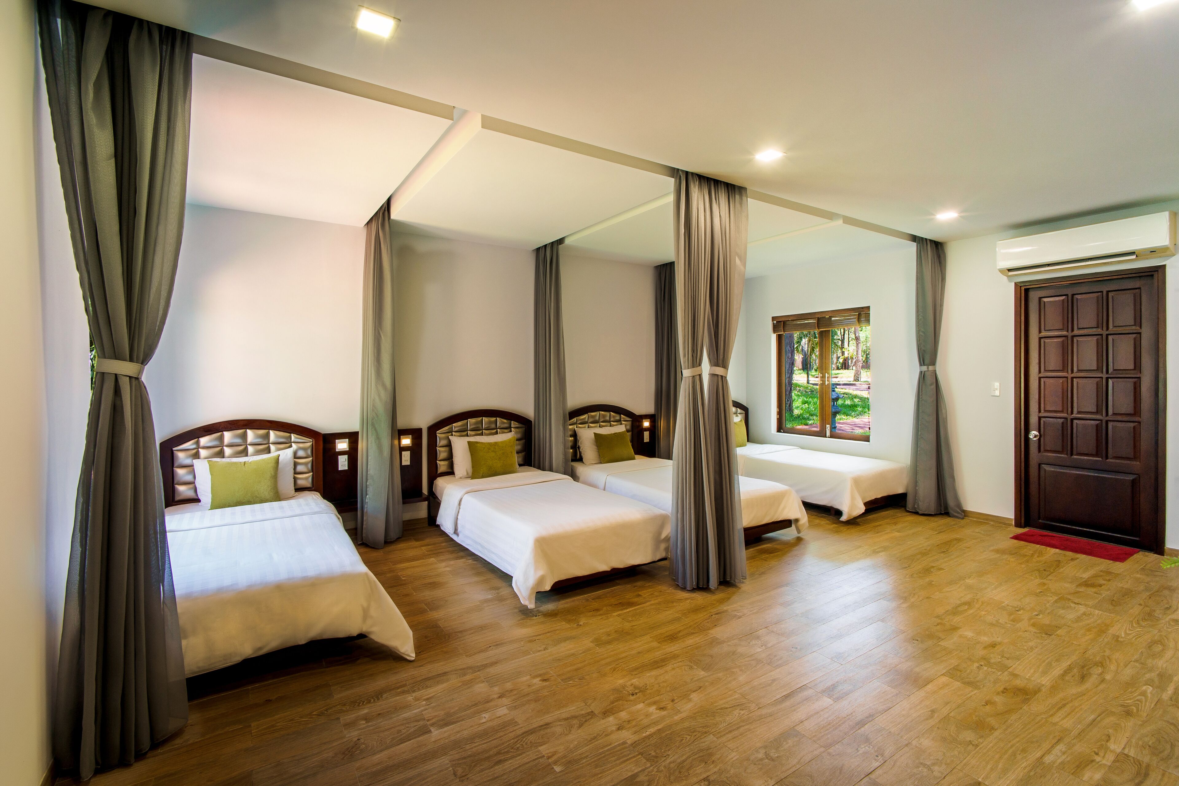 Ein Hotelzimmer mit drei Einzelbetten, Holzboden, einem großen Spiegel und Blick ins Freie.