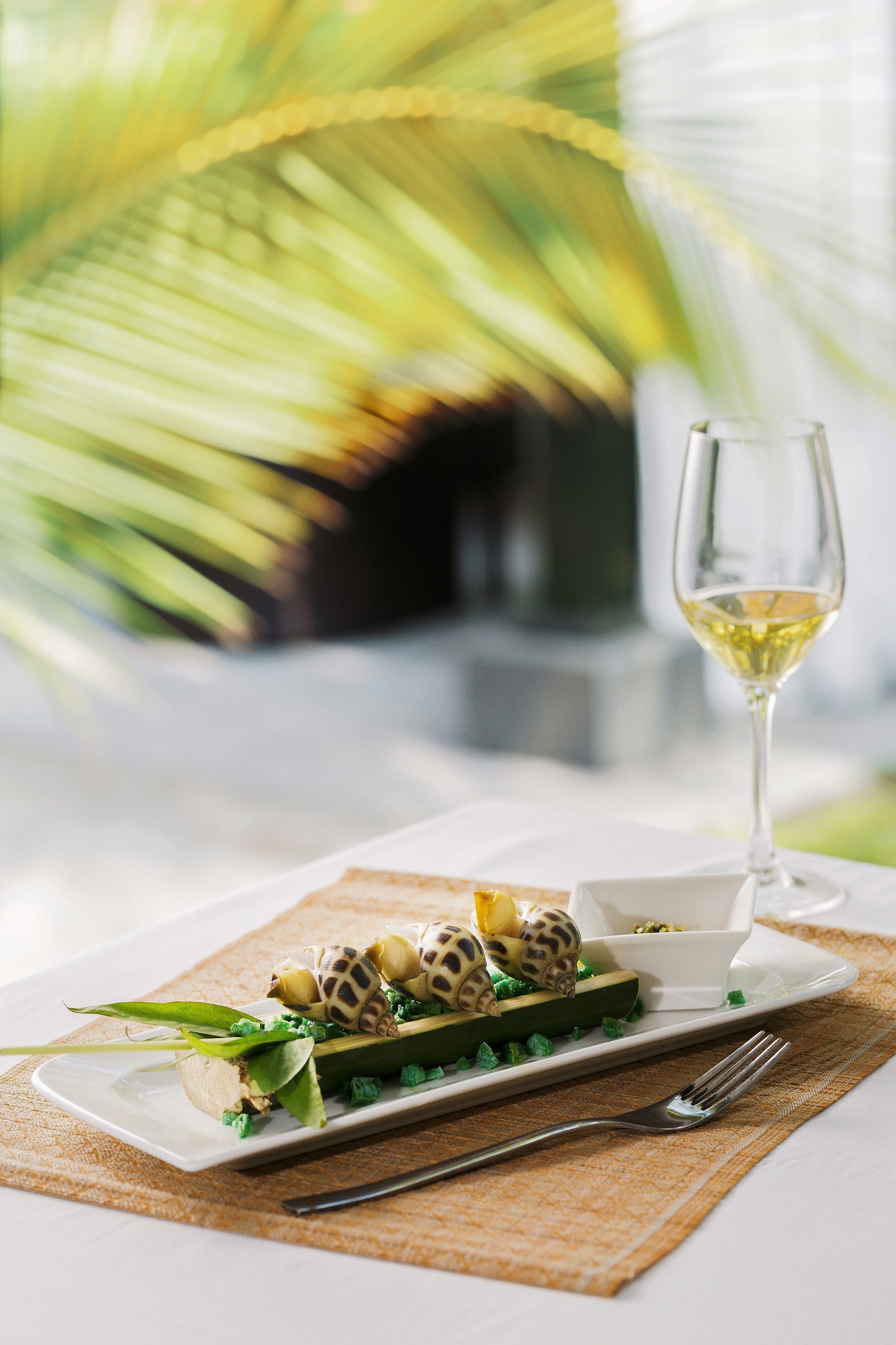 Une table à manger avec une assiette blanche, une fourchette et un verre de vin blanc.