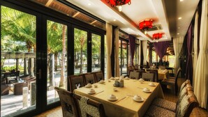 Un restaurante con amplios ventanales, una larga mesa dispuesta para comer y vistas a palmeras.