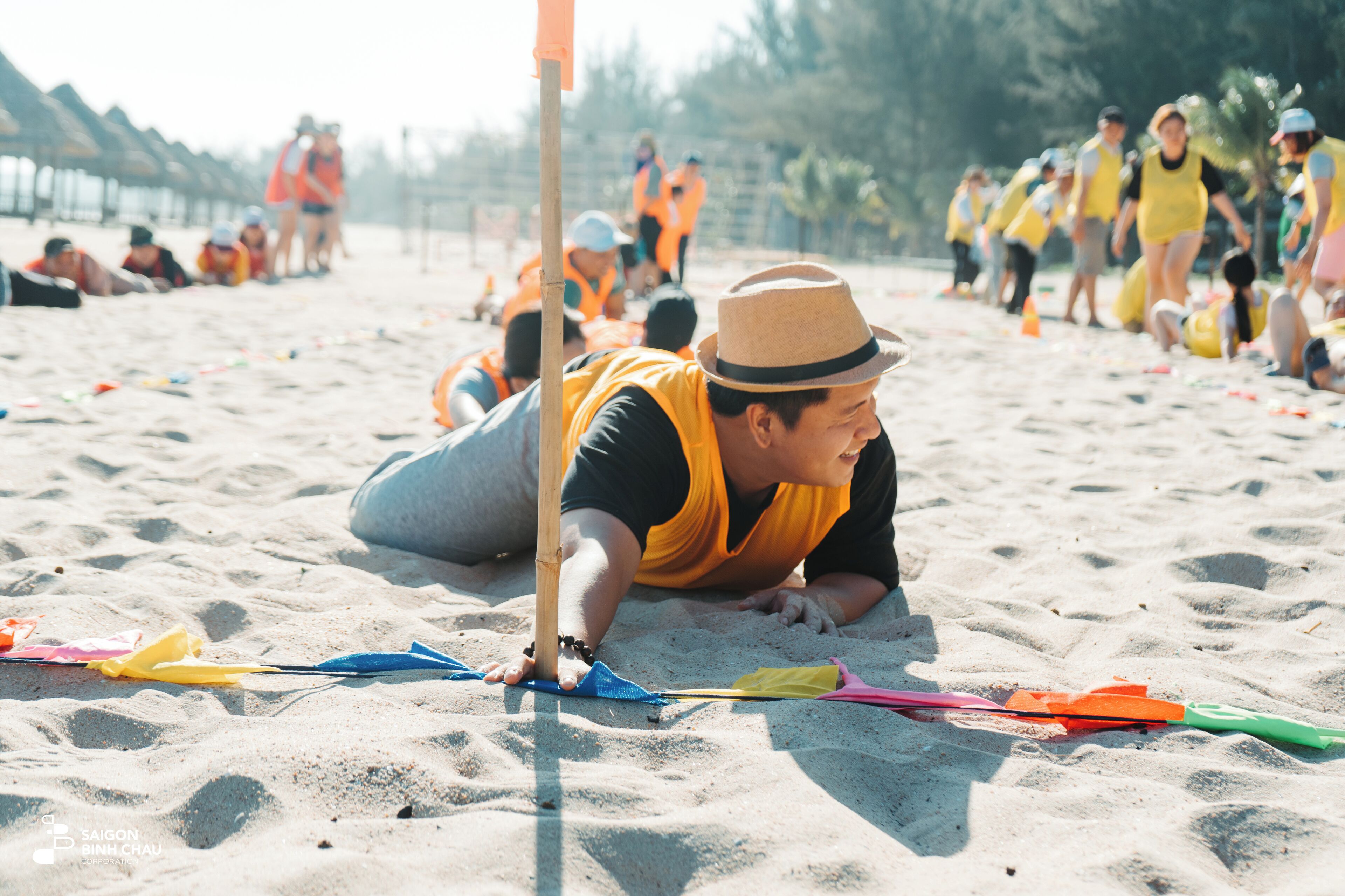 A sandy beach with people in orange vests, some lying down and others standing.