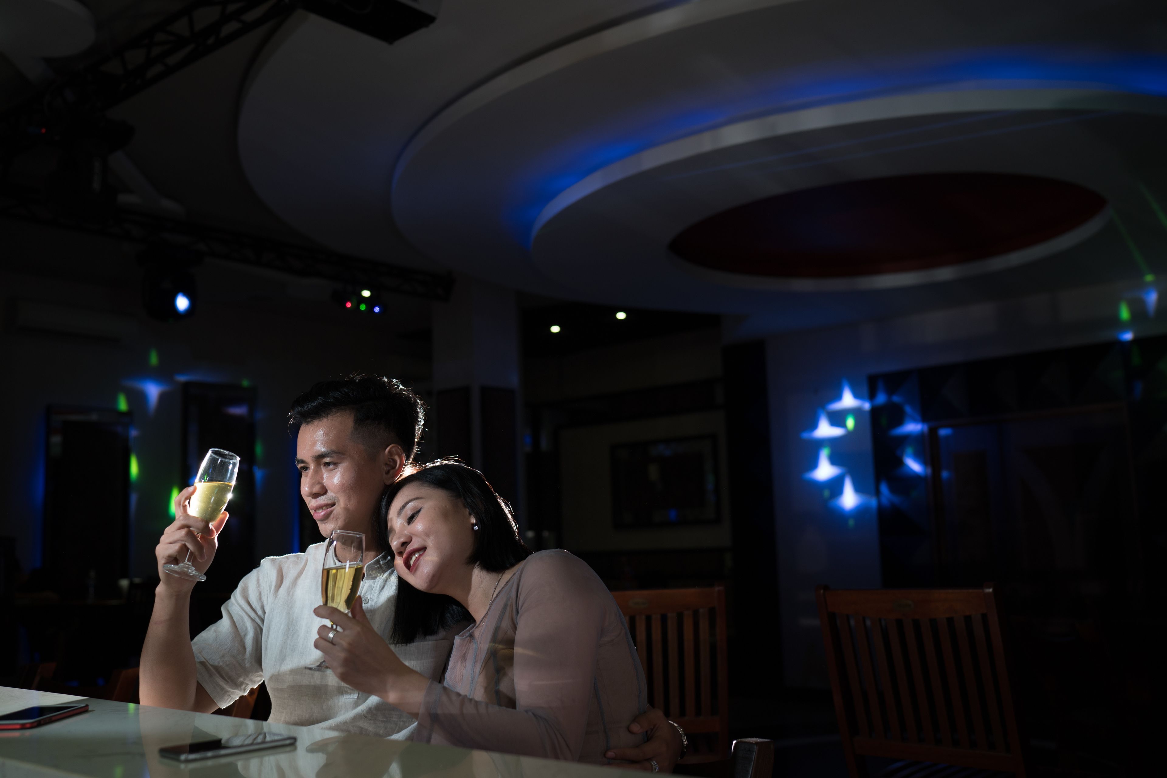 A dimly lit restaurant interior with a couple seated at a table, holding glasses of wine.
