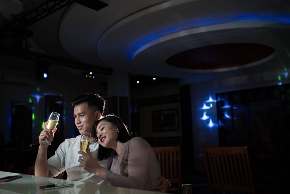 A dimly lit restaurant interior with a couple seated at a table, holding glasses of wine.