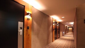 A hotel corridor with wooden doors, numbered room signs, and a carpeted floor. - Designers Hotel The Rich (Goyang)