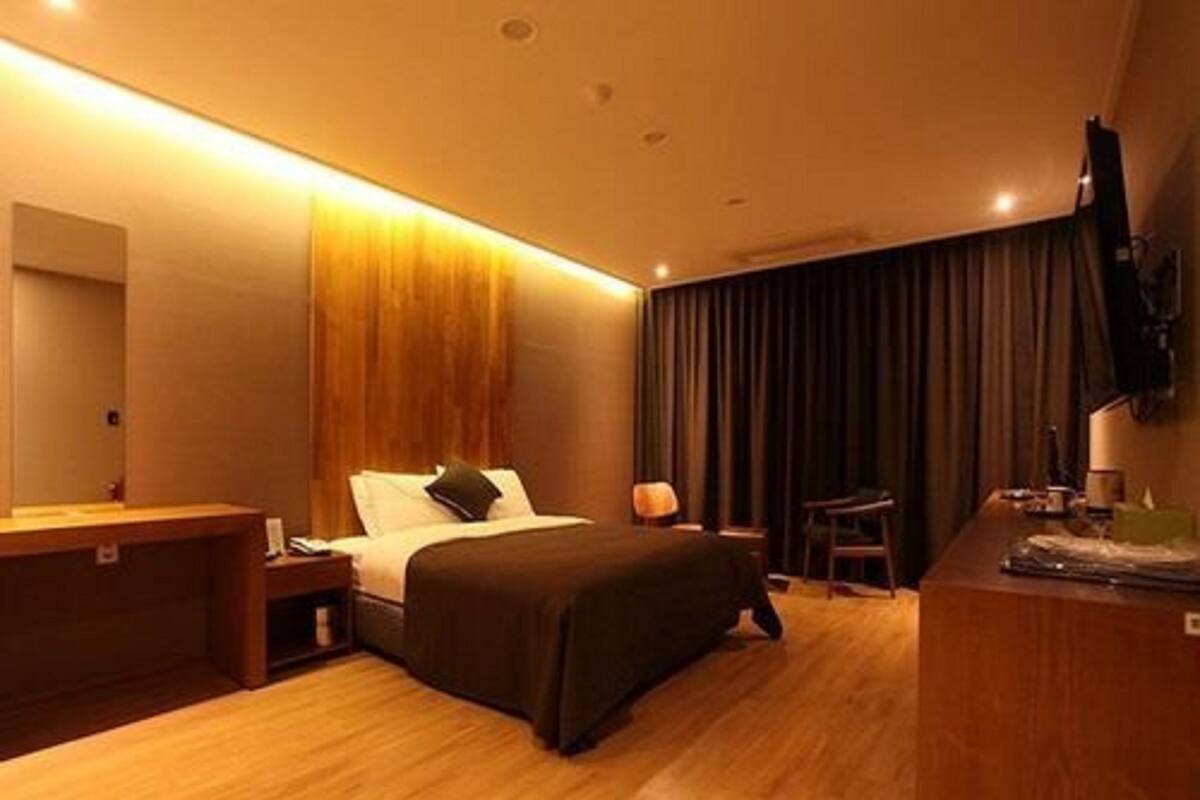 A hotel room with a bed, bedside table, lamp, TV, and a wooden desk.