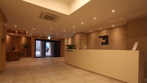 A hotel reception area with a modern design, featuring a reception desk, a large glass door entrance, and a tiled floor. - Designers Hotel The Rich (Goyang)