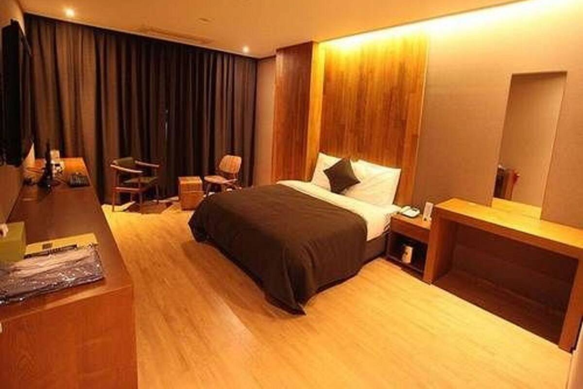A hotel room with a bed, bedside table, chair, desk, and a mirror.