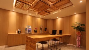 A modern reception area with a wooden reception desk, three bar stools, a coffee machine, a TV, and a potted plant. - Designers Hotel The Rich (Goyang)