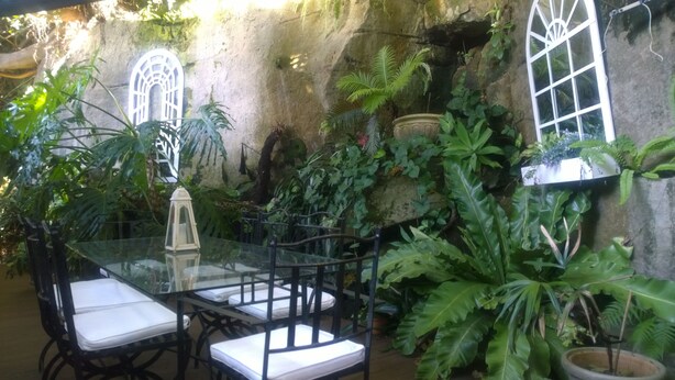 A glass table with chairs in a lush, green outdoor area with stone walls and large windows. - Linley House (Linley Point)