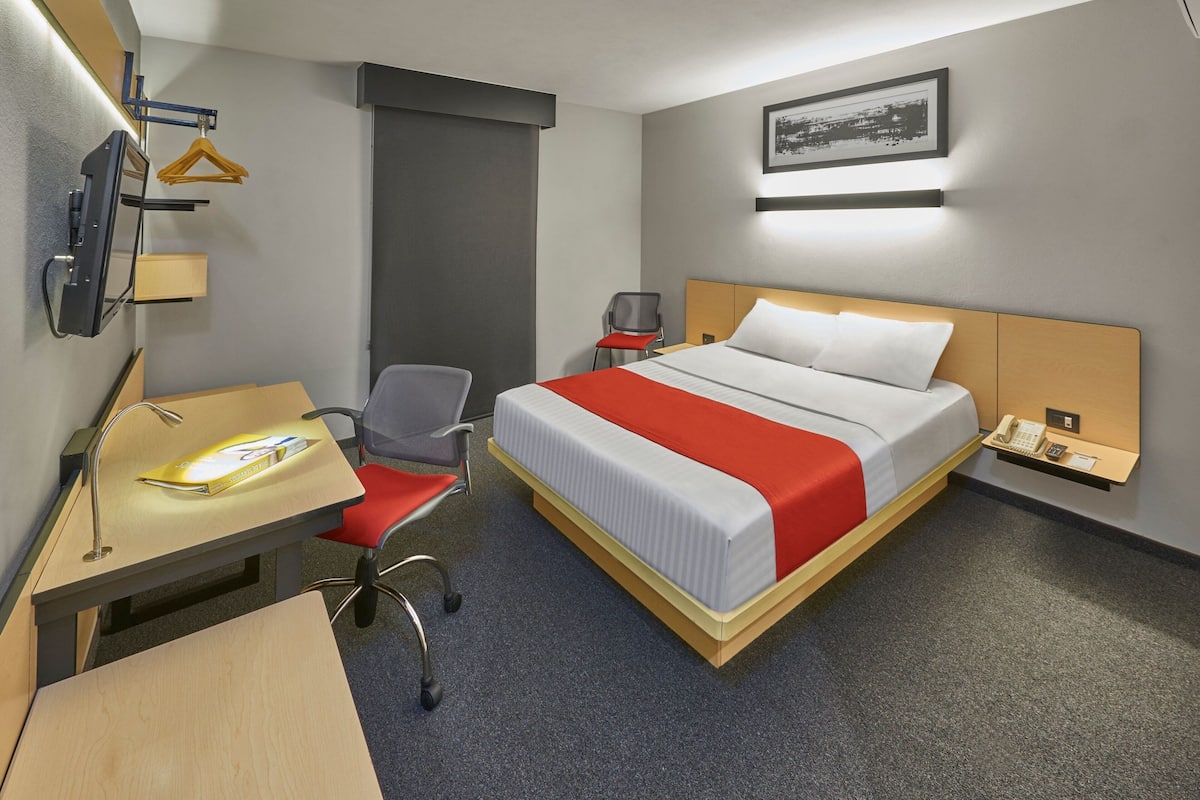 Habitación de hotel con cama, escritorio, silla y una pequeña mesa con teléfono.