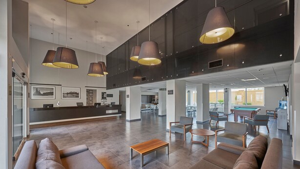 Un vestíbulo amplio con muebles modernos, un mostrador de recepción y una mesa de billar al fondo.