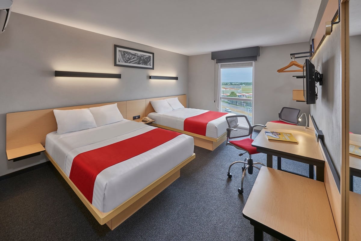 Habitación de hotel con dos camas, un escritorio, una silla, un televisor y una ventana con vistas a la ciudad.