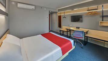 Habitación de hotel con cama, escritorio, silla, televisor y espejo.
