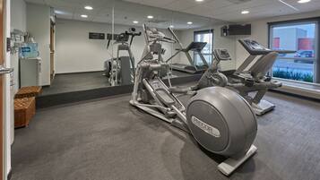 A gym with various exercise equipment, a water dispenser, and a large window with a view of the outside.