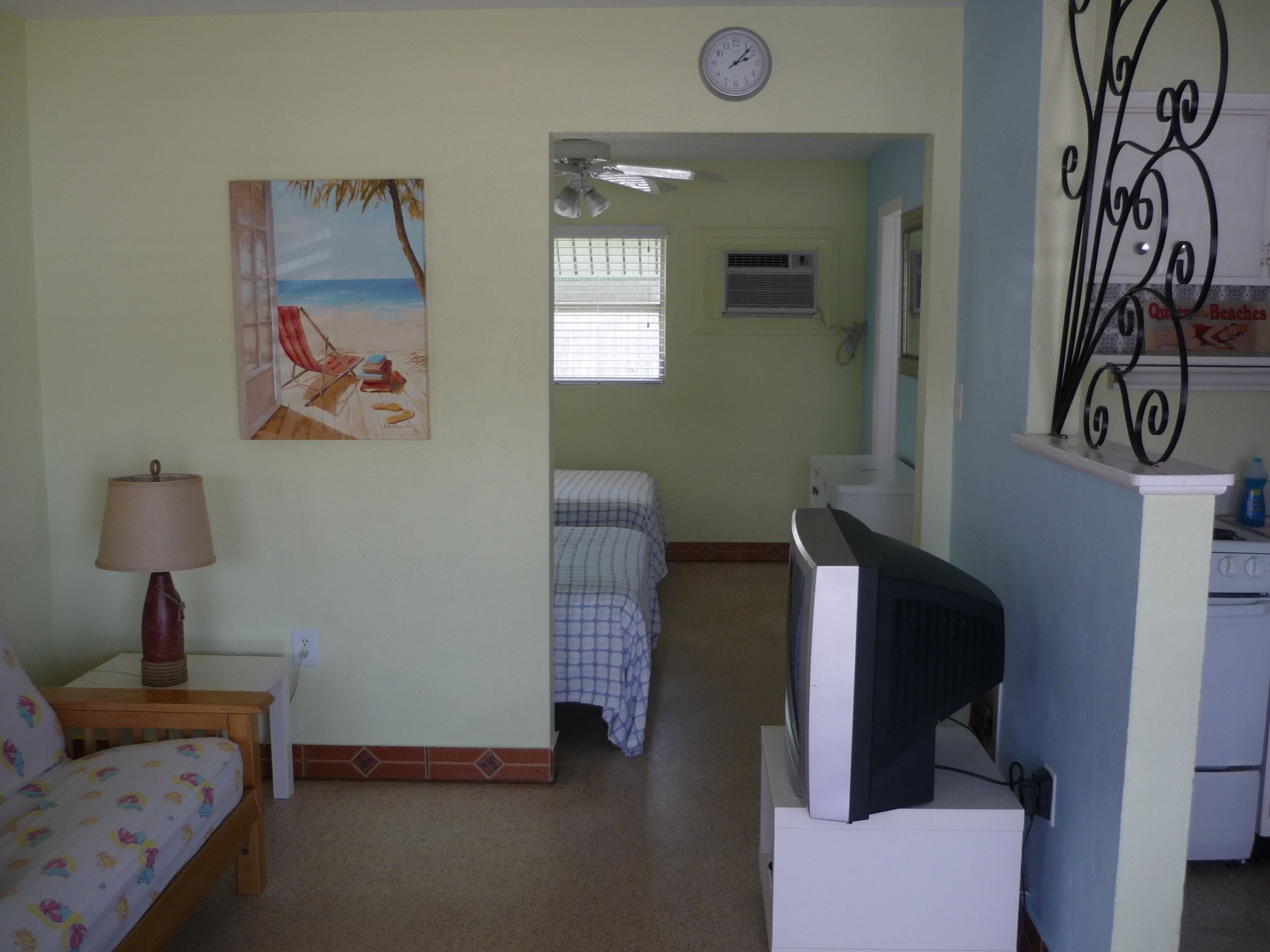 Una stanza con un letto, una televisione, un quadro, una sveglia e una finestra.