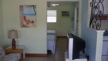 Una stanza con un letto, una televisione, un quadro, una sveglia e una finestra.