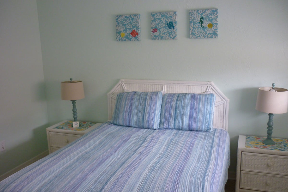 A bedroom with a bed, two nightstands, and three wall-mounted artworks.