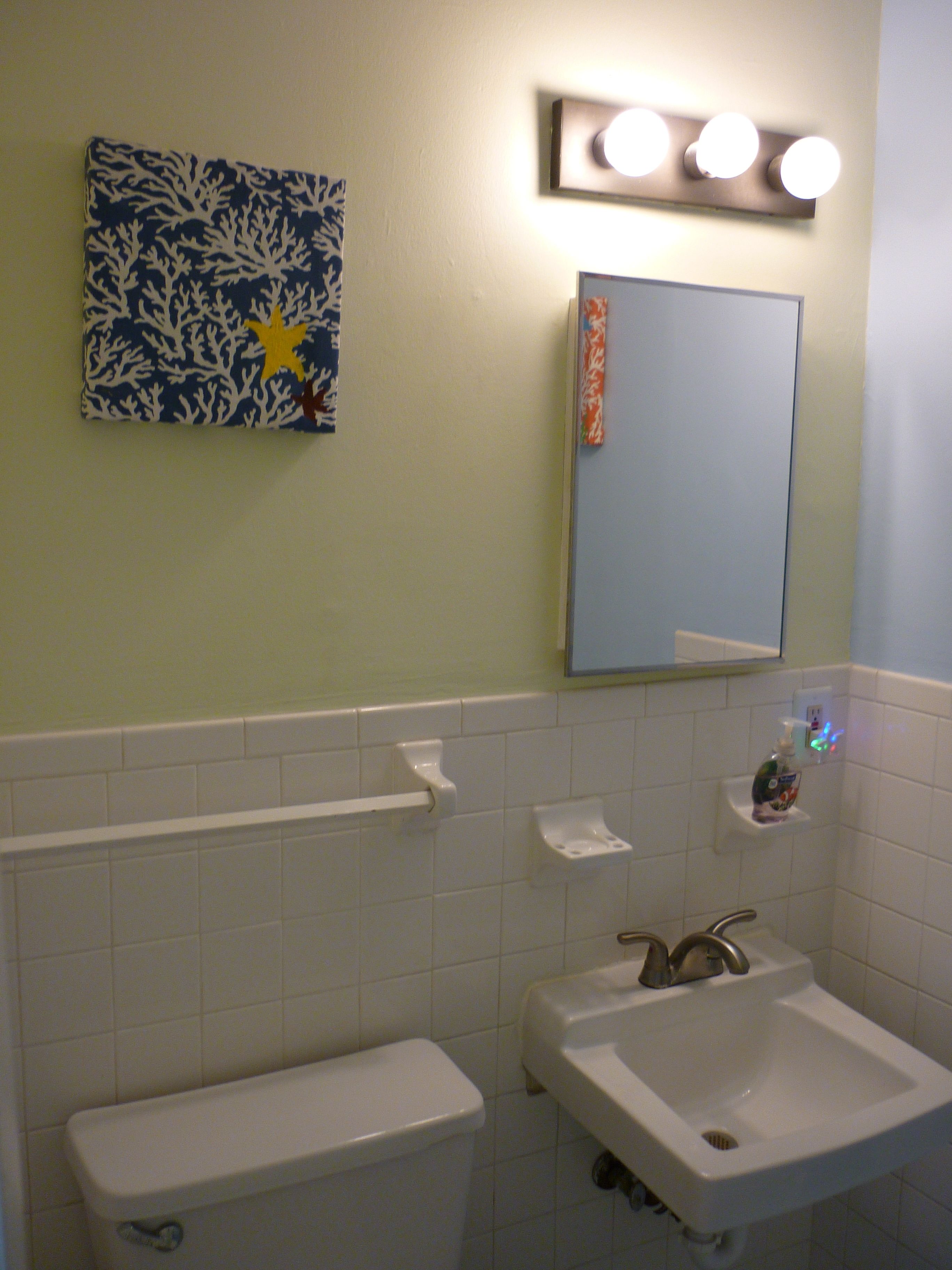 A bathroom with a toilet, sink, and a mirror with lights above.