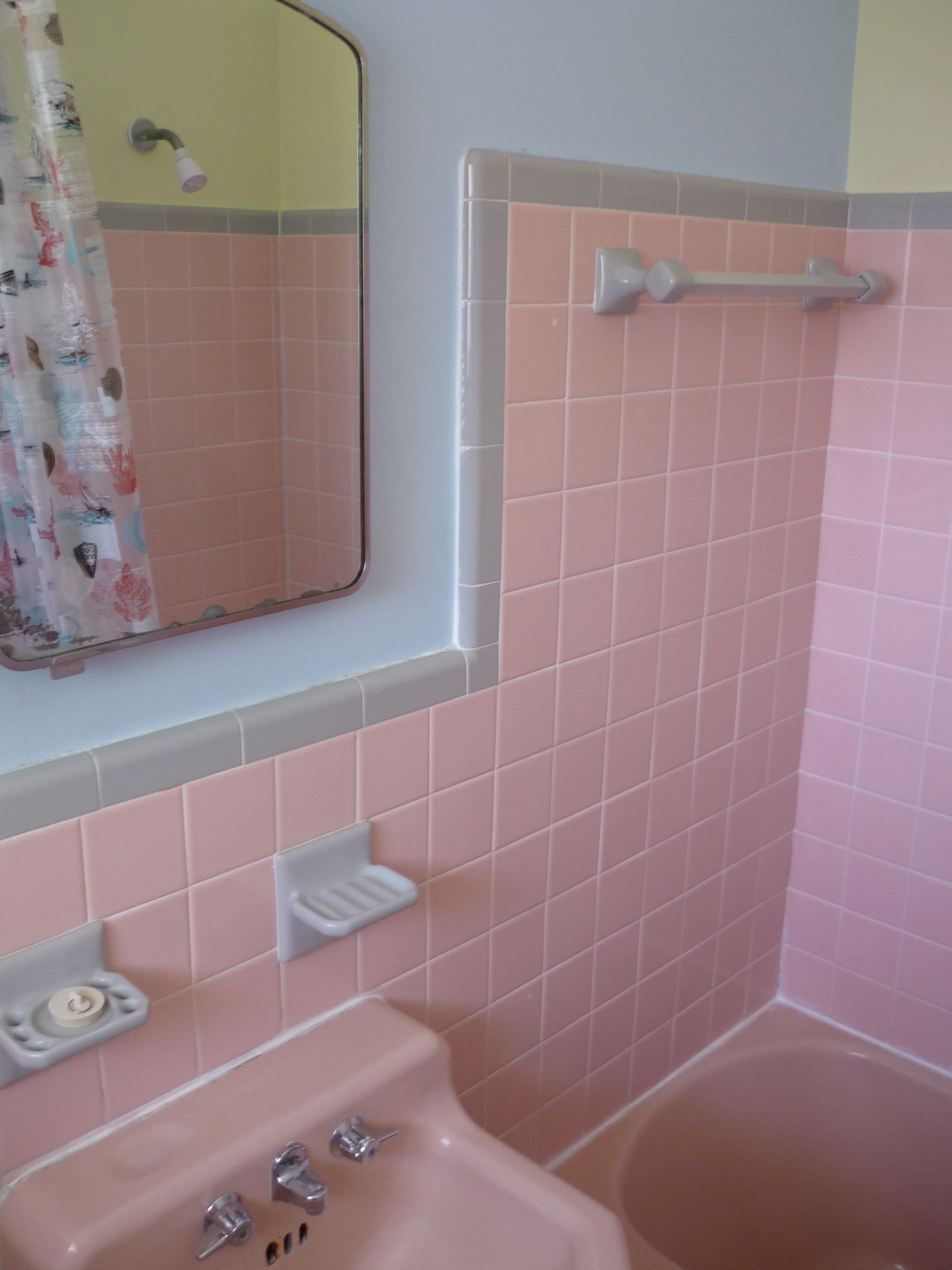 Ett badrum med rosa kakel, ett handfat, en spegel och en duschhörna.